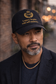 Classy Black man wearing black baseball cap with gold “Legacy begins with self-mastery” embroidery in urban setting